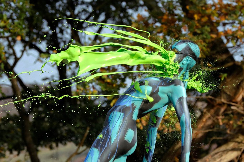 Bodyart-Künstler Jörg Düsterwald ist mit einem unbekleideten, bunt bemalten Fotomodell auf einer Waldlichtung und schüttet der Frau für ein neues Kunstexperiment flüssige grüne und blaue Farbe über ihren Körper